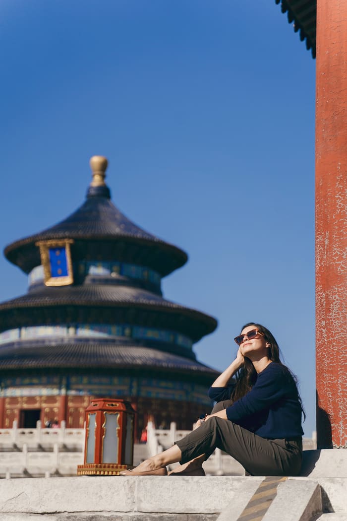 Viajera relajada con gafas de sol sentada frente al Templo del Cielo en Pekín, un monumento imprescindible en un viaje a China.