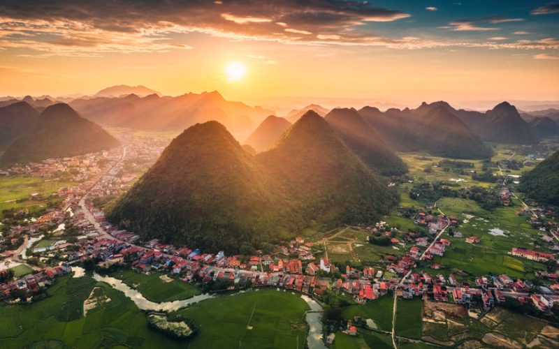 Vista aérea del amanecer en Yangshuo, China, mostrando colinas de karts, campos verdes y un pueblo tradicional al sol.